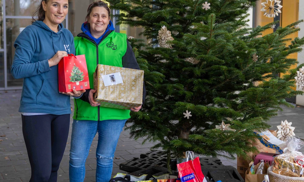 Das Bild zeigt zwei Frauen vor einem Weihnachtsbaum sowie viele Spenden für das Tierheim in Form von Futter oder Spielzeug.
